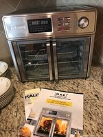 Front view of Kalorik Maxx air fryer oven on countertop with recipe book and instruction manuals laid in front.