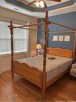 Full view of queen size wooden canopy bed with mattress in a bedroom, showing four turned posts and connected rails forming a canopy frame.