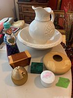 Photo of assorted trinket boxes, yellow vase, pitcher and basin, and painted wooden statue on a table.