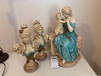 Photo showing the full set of two female busts and one mother-child statue on a tabletop.