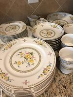 Set includes multiple stacks of plates in various sizes, bowls, cups, cream pitcher, and sugar bowl, all with matching floral patterns and gold trim.