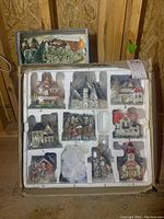 Box of nine lighted Christmas houses in white foam packaging, front view showing individual houses in slots.