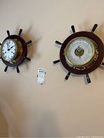 Both wood and brass ship's wheel wall clock and barometer mounted on beige wall.