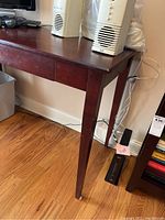 Side and leg view of the wooden desk showing dark finish and single leg, positioned on a wood floor.