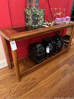 Front view of wooden console table showing smoke glass inset on the top and lower shelf with electronic devices beneath.