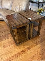 Pair of wooden end tables placed side by side on hardwood floor next to a beige sofa. Both tables have plank-style tops with metal corner braces and lower shelves.