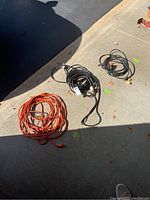 Three heavy duty extension cords laid out on concrete floor, showing orange and black cords of different lengths