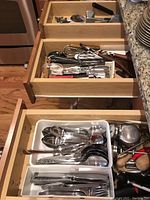 Flatware and kitchen utensils arranged in kitchen drawers showing spoons, knives, whisks, and other tools