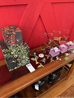 Photo of two decorative boxes and a set of colorful hummingbird ornaments and gold-tone metal holders arranged on a wooden surface against a red wall.