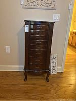 Front view of wooden jewelry cabinet with eight drawers and curved legs.