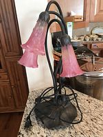 Front view of table lamp showing three pink flower-shaped glass shades attached to black metal stems.