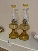 Pair of full amber glass oil lamps on shelf, showing overall shape and color.