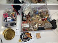 Wide view showing pins, coins, box with pins, money clip, lighters, and black fabric hat on a reflective surface