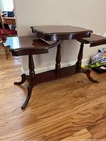 Full view of the three-tier table showing the entire structure with three shelves, turned supports, and curved legs on wood floor.