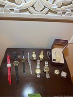 10 watches displayed on surface; red leather banded women's watch and multiple men's watches with metal and leather bands, some watch faces without bands