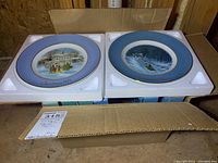 Two Wedgwood Avon Christmas collector plates with blue border and gold trim in original white foam packaging in a cardboard box