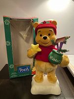 Overall front view of the Winnie The Pooh animated Christmas display figure with original box visible in background