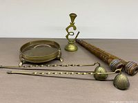 All items arranged on a flat surface: two wooden textile spindles, two brass candle stuffers, brass candleholder, and brass incense burner.