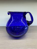 Front side view of a round cobalt blue glass jug showing its handle and bubble details in the glass.