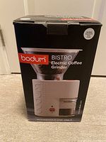 Photo of the original box of the Bodum Bistro electric coffee grinder in off white color with product image and branding.