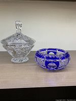 Pair of crystal dishes on shelf: clear lidded pinwheel candy dish and blue cut-to-clear ashtray