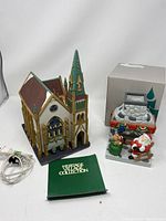 Full view of Dept 56 Christmas church with light cord, green booklet, and Partylite tea light holder depicting Christmas scene with Santa Claus.
