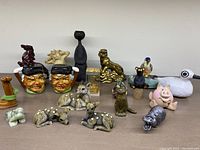 Wide view of assorted figurines and salt & pepper shakers on a beige surface against white background showing all items in the lot.