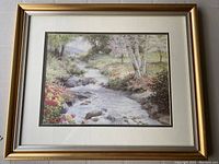 Full view of the framed print showing a river in a natural landscape with trees and flowers.