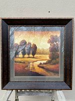 Framed landscape print showing autumn trees and a river, in a dark brown textured frame with double mat.