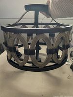Hand held view of circular wrought iron frame light fixture with painted driftwood loops pattern, held from top mounting rod.