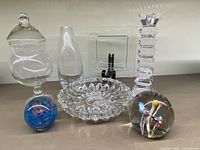 Full set of mixed glass and crystal decor including apothecary jar, vase, slumped plate, ashtray, candleholder and two paperweights shown together.