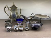 Full lot of 11 silver plated serving pieces including coffee pot, sauce boat, pedestal cake stand, covered butter dish, sugar bowl set, creamer, and blue glass liner bowl.