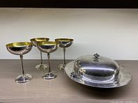 Four silverplated champagne goblets and a warming server with lid on a flat surface, showing overall look and condition.
