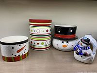 Front view showing all four ceramic items: striped Crate & Barrel canister, snowman head plant pot, snowman head bowl, and coaster holder snowman with coasters.