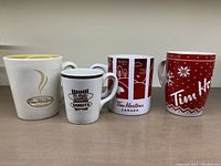 Front view of four Tim Hortons mugs with different designs and colors placed side by side