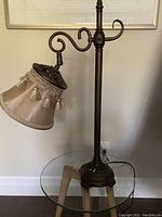 Full view of vintage style metal side arm lamp on clear glass table, showing overall shape and structure.