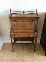 Full view of child size antique secretary desk showing carved front panel with bird motif, drawer with brass handles, and wooden legs.