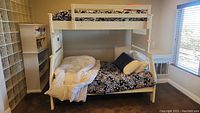 Full side view of white wooden bunk bed set up with black and white floral bedding and white comforter on lower bunk.