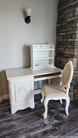 Full view of the vintage cream-colored wooden desk with small cream-colored shelf on top, and matching upholstered chair.