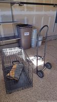 Photo showing the metal furniture dolly, black metal dog crate with a pad inside, and some barbell weights stacked in the background.