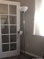 Front view of the nickel toned floor lamp with two lamps, one large upward-facing lamp with white glass shade, and one smaller adjustable lamp attached to the pole.