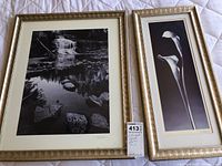 Two framed black and white prints side by side, waterfall scene on left, calla lilies on right, shown on a white quilted surface.