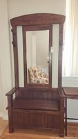 Full view of wooden hall tree showing bench seat, back with mirror, and coat hooks.