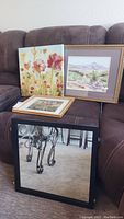 All items displayed on brown couch: floral canvas, two framed prints, and black framed square mirror.