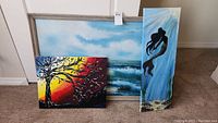 All three original acrylic paintings shown together. One large framed ocean wave painting, tree painting with sunset colors, and narrow mermaid silhouette painting.