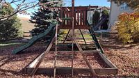 Overall front view of the wooden playground structure with sandbox, slide, ladder, swing set and tire swing visible