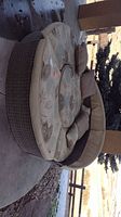 Full view of round sectional showing rattan base and floral cushions with pillows outdoors on concrete surface