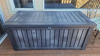 Front angled view of the dark gray plastic outdoor storage box with wood-like panel design and lock loop.