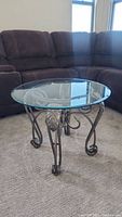 Round side table with beveled glass top shown beside brown couch.