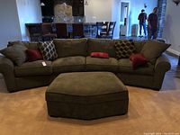 Front view of olive green two-piece sectional sofa with one of the ottomans in front, arranged in living room.